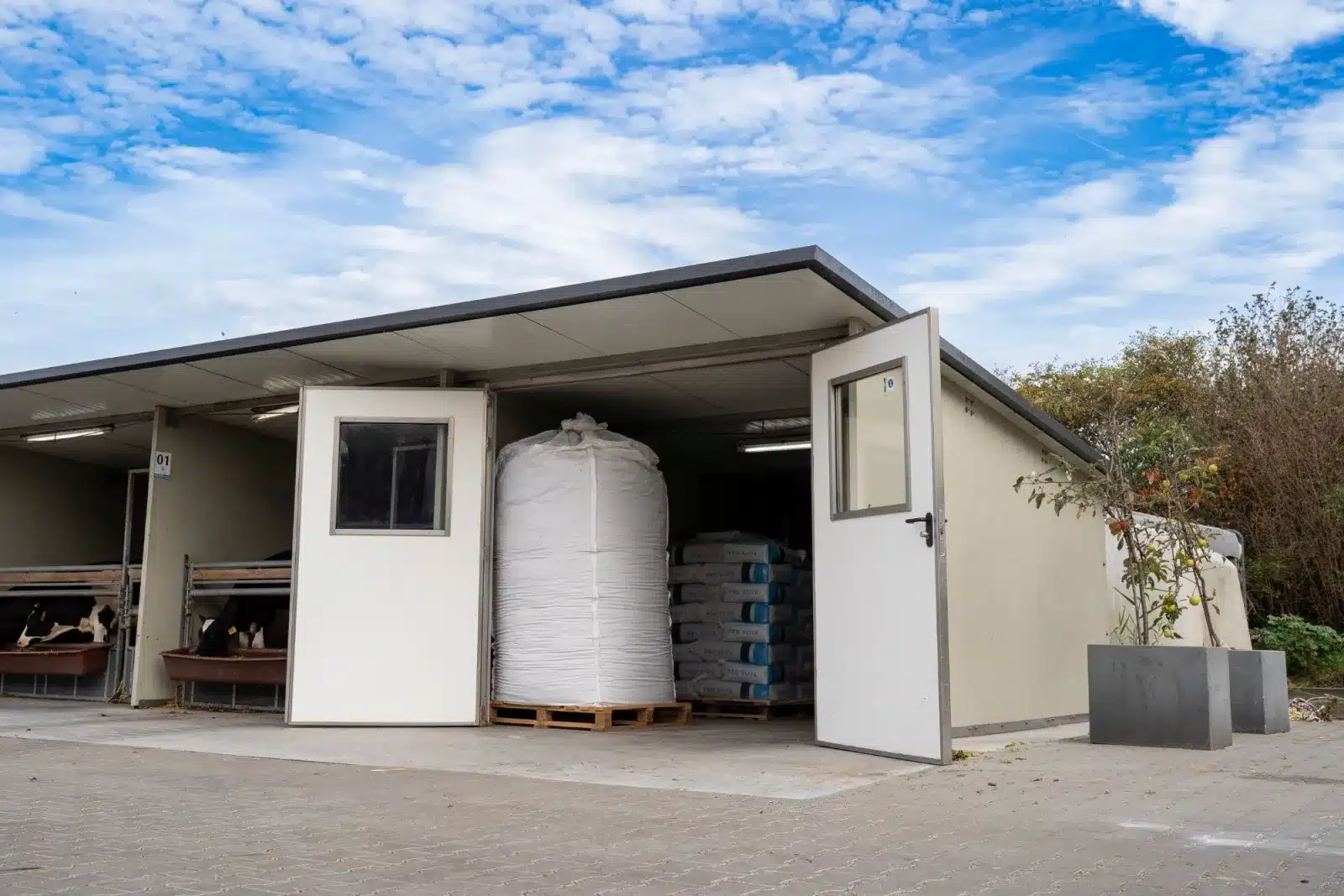 Afdeling van een Optima Klima Stal met de dubbele deur open, ingericht als opslag met een big bag en pallets voer