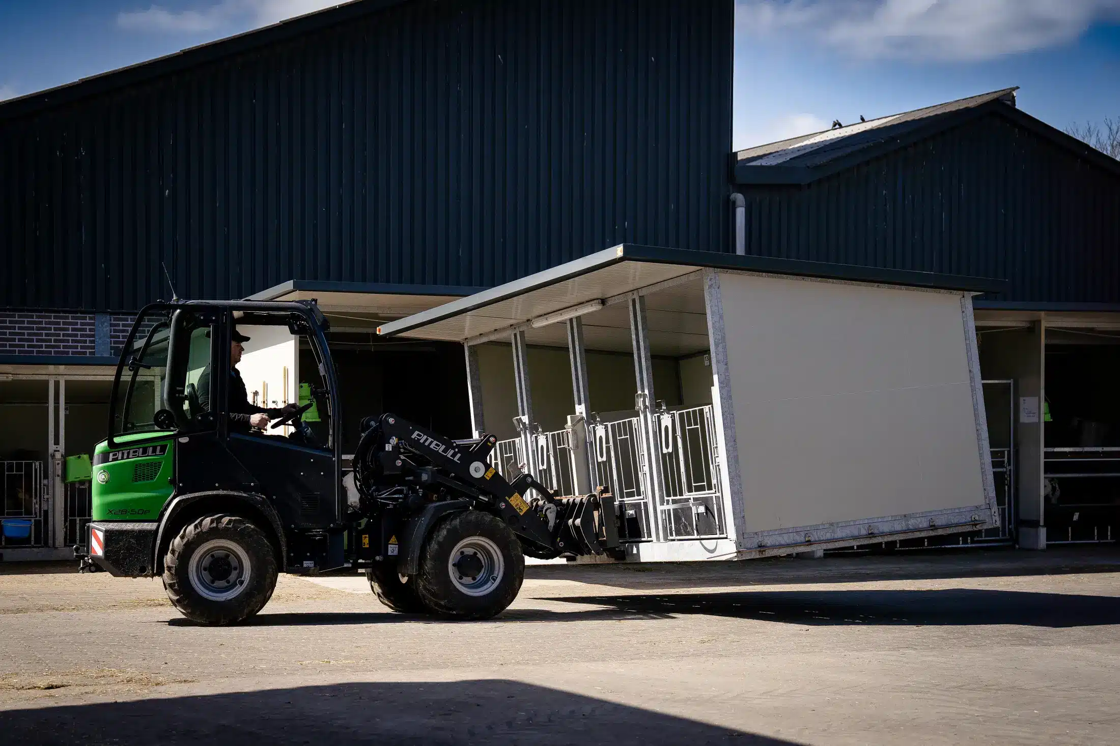 Een shovel rijdt een Quattro Kalverbox XL over het erf voor de stal